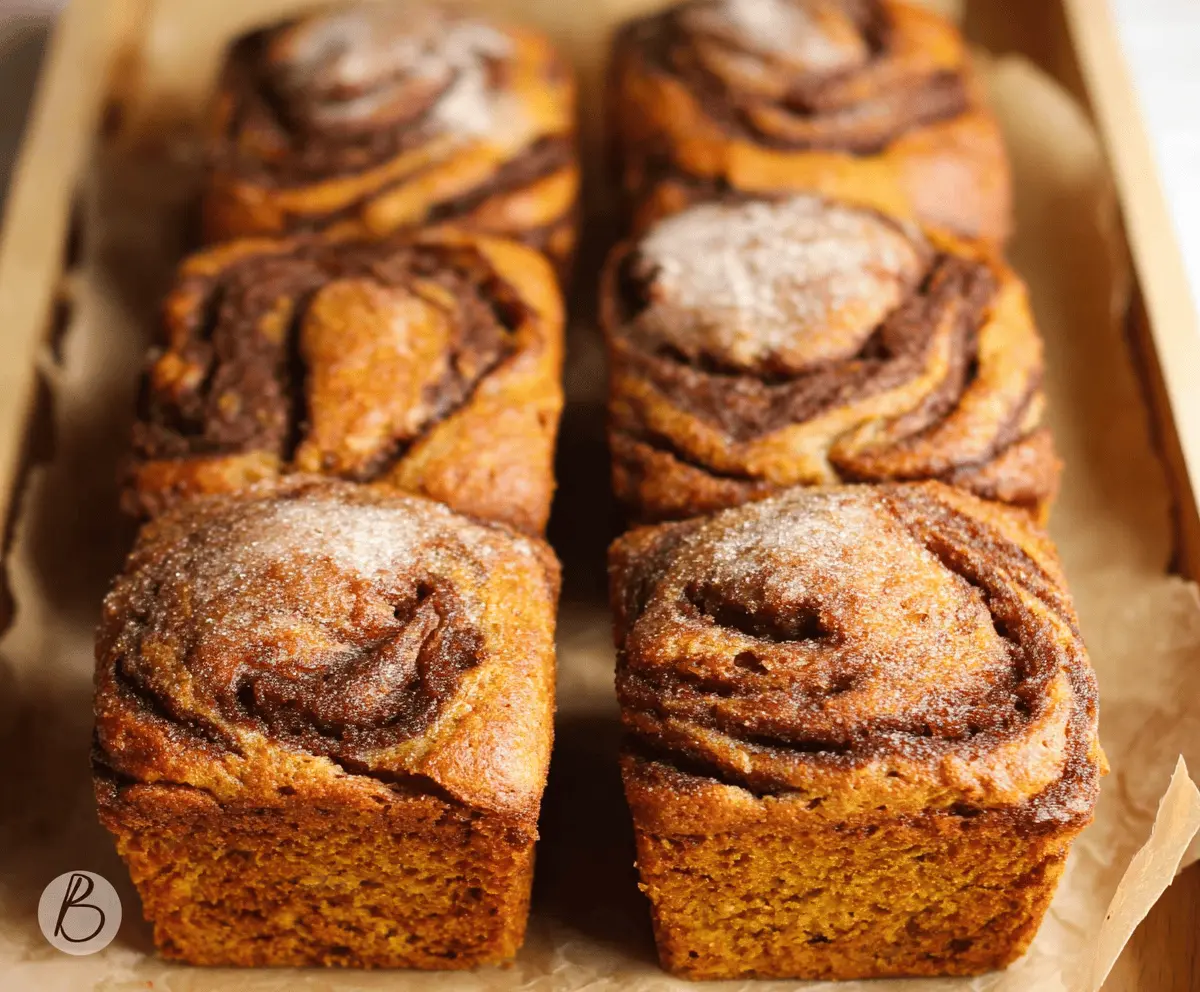 Mini loaves of cinnamon swirl pumpkin bread topped with a sprinkle of cinnamon, featuring a moist, flavorful pumpkin bread with a cinnamon swirl inside, perfect for fall baking.