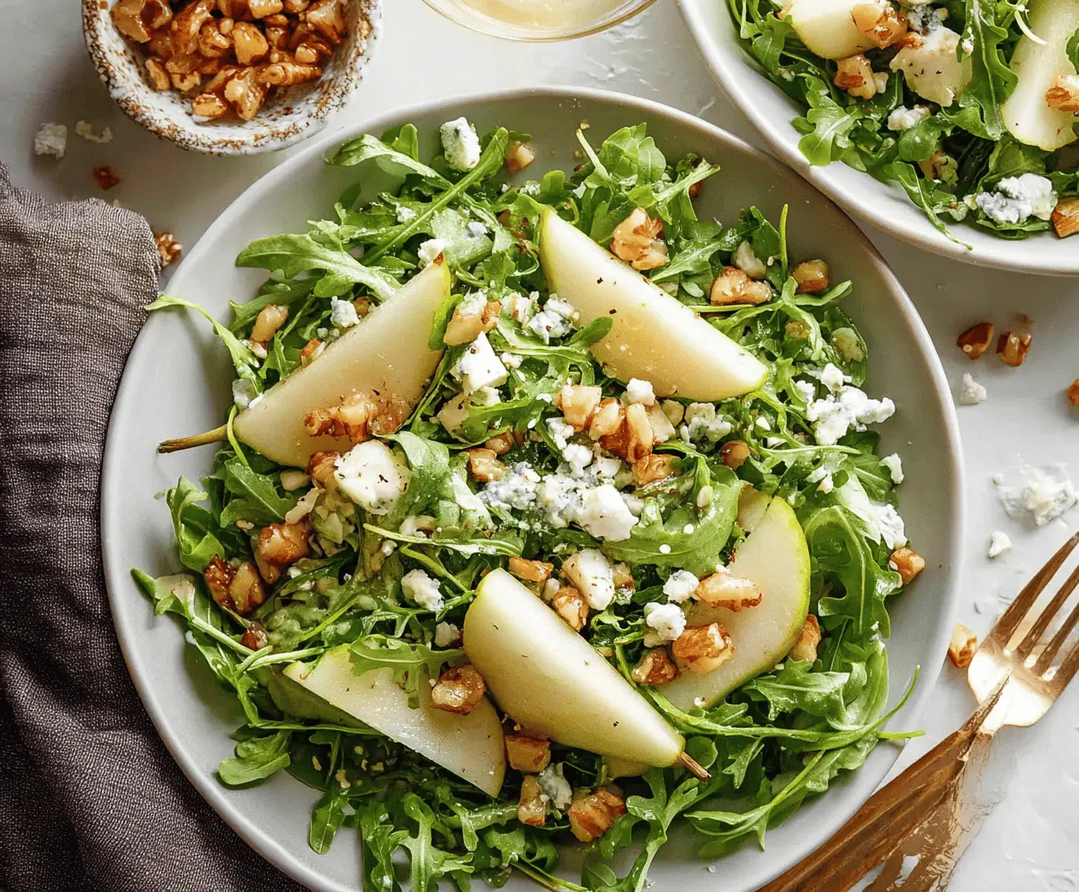 Fresh pear and peppery arugula salad topped with walnuts and crumbled cheese, served in a white bowl.