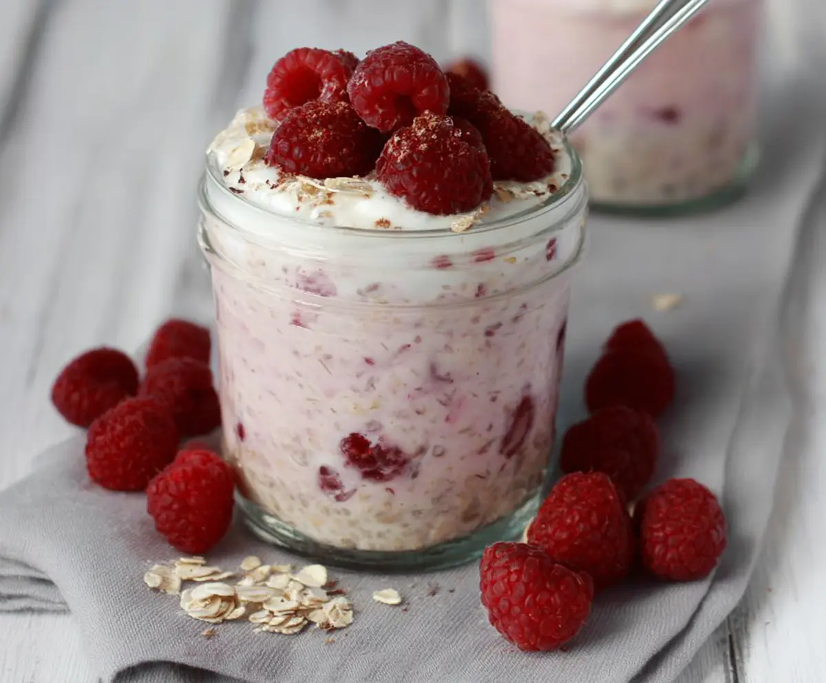 Creamy raspberry overnight oats in a glass jar topped with fresh raspberries and mint leaves for a healthy breakfast.