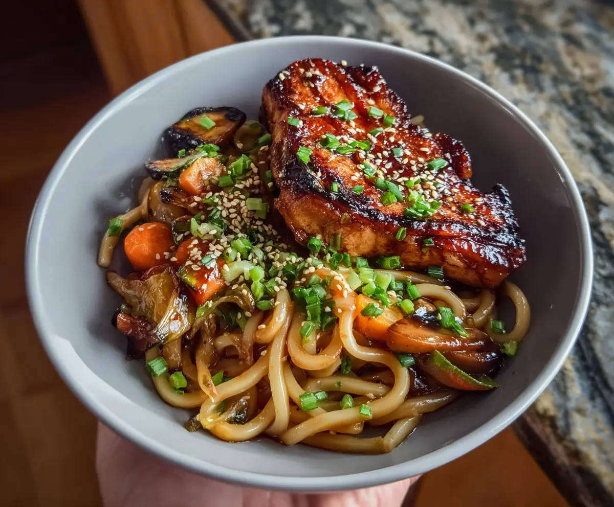 Delicious veggie udon noodles topped with fresh vegetables and savory sticky glazed pork chops ready to serve.