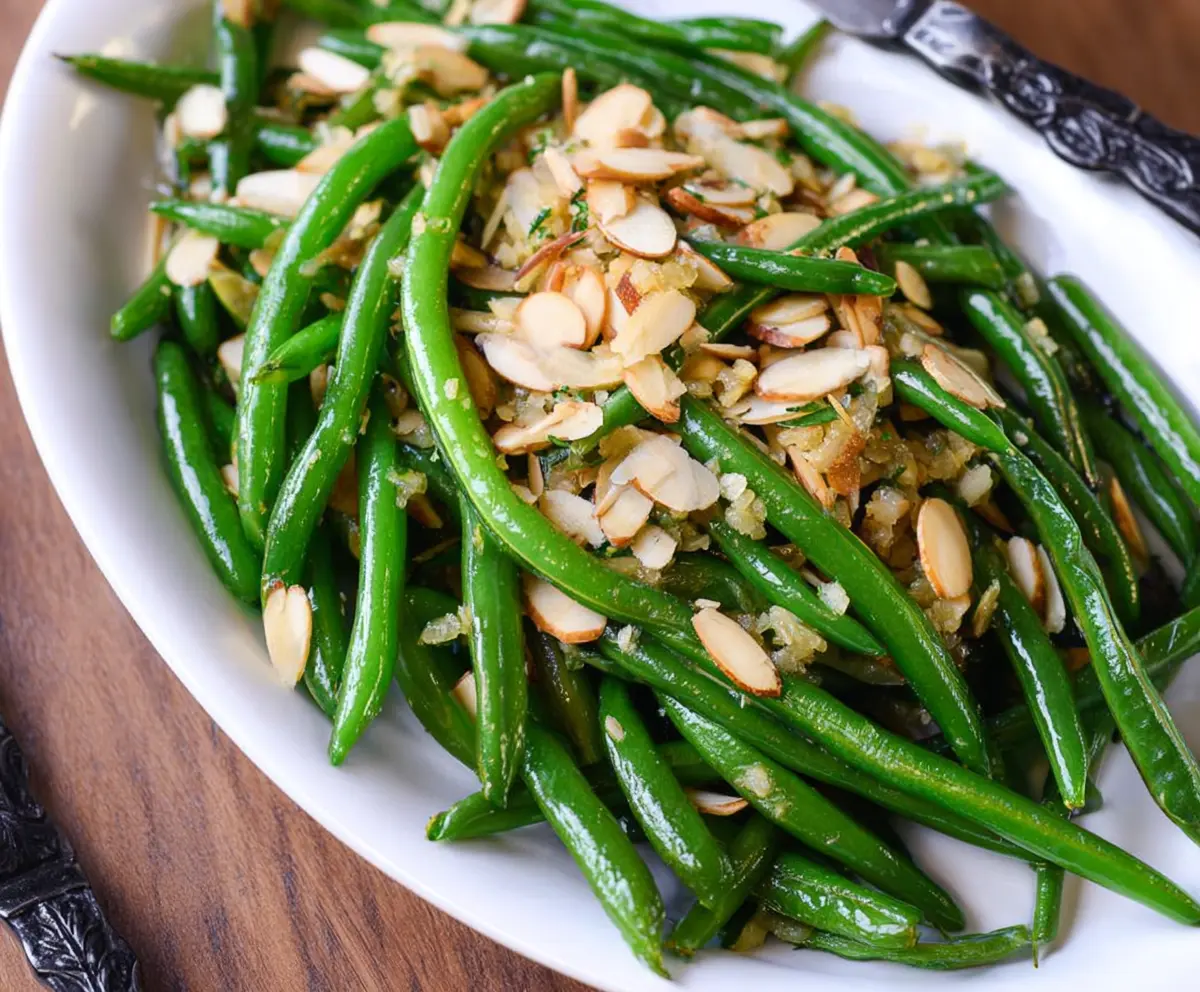 Fresh green bean almondine dish garnished with sliced almonds on a white plate.
